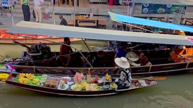 Ratchaburi, Tayland, 7 Aralık 2025, taze meyve ve atıştırmalıklarla dolu renkli tekneler Damnoen Saduak 'ın hareketli yüzen pazarında süzülüyor..