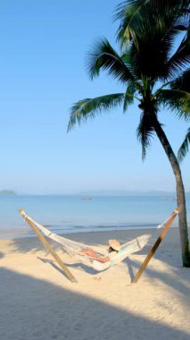 Koh Phayam 'da sakin bir sahil mükemmel bir kaçış sunuyor. Bir kadın, Tayland 'ın çarpıcı manzaralarıyla çevrili sallanan palmiyelerin altında hamakta uzanırken, yumuşak okyanus esintisinin tadını çıkarır.