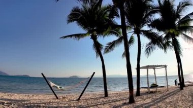 Altın kumlar Koh Phayam Tayland 'ın sakin kıyı şeridi boyunca uzanır, uzun palmiye ağaçları hafif esintide dans eder. Konuklar hamaklarda dinlenirken dalgalar sahilde usulca tur atıyor..