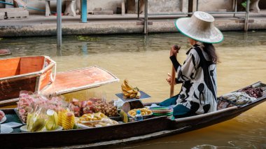 Tayland 'daki Damnoen Saduak Yüzen Pazarı' nın dinamik atmosferini keşfedin. Satıcılar teknelerinden taze meyve ve yerel lezzetler satarken, suyun üstünde renkli bir manzara beliriyor..