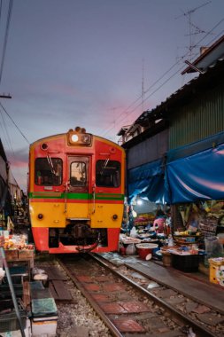 Tayland 'daki Maeklong Demiryolu Pazarı' ndan geçen bir tren yaklaşıyor ve satıcılar mallarını sergiliyor. Bangkok, Demiryolu Pisti 'ndeki Taze Pazar. Gün doğumunda ünlü bir demiryolu pazarı.