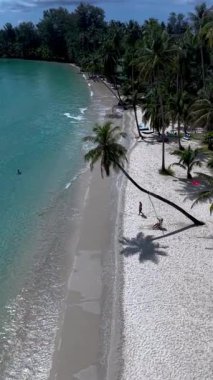 Tayland 'daki Koh Kood Adası' nın güzelliğini yaşayın, yumuşak beyaz kum, canlı turkuaz sular, sallanan palmiye ağaçları, sahildeki bir palmiye ağacının altında sallanan bir çift.