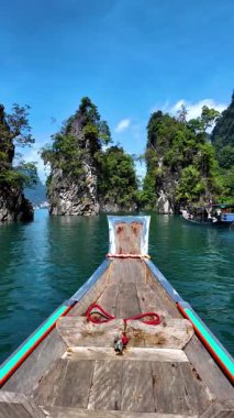 Tayland 'daki Khao Sok' un sakinliğini, büyüleyici kireçtaşı kayalıkları ve yemyeşil yeşilliklerle çevrili temiz zümrüt sularında süzülen ahşap bir tekne gibi hissedin. Doğa mucizesi bekliyor..