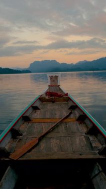Geleneksel bir ahşap tekne sabahın erken saatlerinde Khao Sok, Tayland 'ın sakin sularında süzülür..