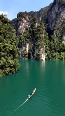 Yüksek uçurumlar ve yemyeşil bitki örtüsüyle çevrili, Khao Sok 'un sakin yeşil sularında yalnız bir tekne süzülüyor. Bu nefes kesici yer Tayland 'ın doğal güzelliğini ve sükunetini gösteriyor..