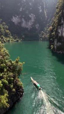 Tayland 'daki Khao Sok Ulusal Parkı' nın dingin güzelliğini keşfedin. Zümrüt sularında süzülen geleneksel bir tekne yüksek uçurumlar ve canlı yeşil yapraklarla çevrili..