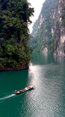 Tayland 'daki Khao Sok Ulusal Parkı' nın dingin sularında, yemyeşil ve yüksek kireçtaşı kayalıkları arasında geleneksel bir tekne süzülüyor. Doğanın dokunulmamış güzelliğini tecrübe et..