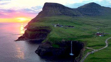 Mulafossur şelalesinin nefes kesen manzarasını deneyimleyin. Okyanusa dökülen büyüleyici Gasadalur köyü, altın saat boyunca yemyeşil araziye yerleşmiştir..