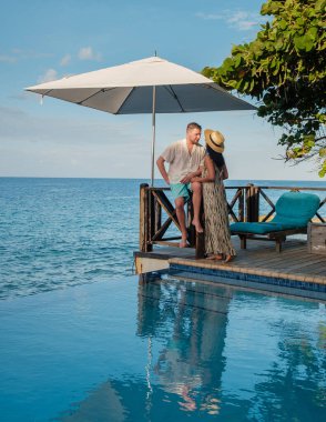 Bir çift, Pietermaai, Curacao 'da havuz kenarında romantik bir anın tadını çıkarıyor. Turkuaz sular, büyük bir şemsiyenin gölgesinde sarmaş dolaş gökyüzünü yansıtır. Tatil için mükemmel..