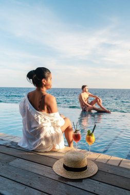 Bir kadın sonsuz havuzun kenarında oturmuş tropikal içkilerin tadını çıkarırken huzurlu bir manzara ortaya çıkıyor. Arka planda güneşin tadını çıkaran bir adam, Curacao 'da tatilin özünü somutlaştırıyor..