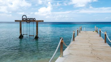 Willemstad, Curacao 'daki Kokomo Sahili' nin sakin manzarasında turkuaz suları temizleyen ahşap bir iskele var. Salıncaklar gevşemeyi davet eder, mükemmel bir tropik kaçış için..