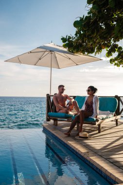 Two people enjoy a tranquil afternoon by the pool, basking in the sun with stunning views of the Caribbean sea. A couple of men and women on vacation in Curacao are relaxing by the pool