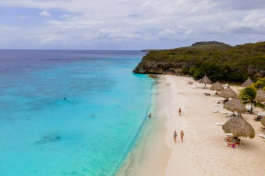 Ziyaretçiler Curacao 'daki Cas Abao Sahili' nin ılık güneşinde güneşlenerek berrak mavi suların ve kumlu sahillerin tadını çıkarıyorlar. Tropikal ortam, Karayip cennetine rahatlama ve eğlenceyi davet ediyor..