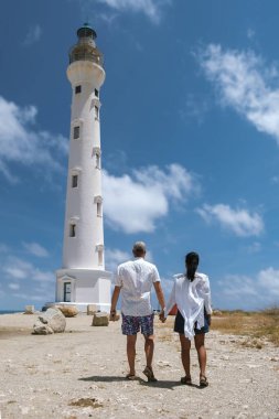 Bir çift el ele yürür Noord, Aruba 'da uzun, beyaz bir deniz fenerine doğru.