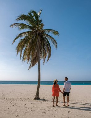 Bir çift el ele tutuşur, Aruba 'daki Kartal Sahili' nin yumuşak kumları boyunca huzurlu bir yürüyüşün tadını çıkarırlar..