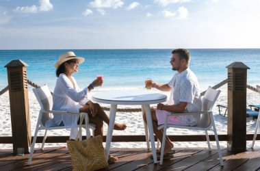 Çift, yumuşak kum ve canlı turkuaz sularla çevrili Divi Sahili sahilindeki bir masada ferahlatıcı kokteyllerin tadını çıkarıyor. Aruba 'da romantik bir tatil için mükemmel bir kaçış..