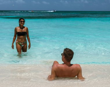 İki arkadaş, Aruba 'daki Palm Beach' te güneşli bir günün tadını çıkarıyorlar. Turkuaz suların yumuşak beyaz kumla buluştuğu yerde. Kahkaha ve neşe, bu Karayip cennetinin canlı güzelliklerine boğulurken havayı dolduruyor..