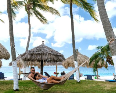 İki arkadaş, Divi Sahili, Aruba 'da palmiye ağaçlarıyla çevrili bir hamakta gevşeyip, ılık güneşin ve serin esintinin tadını çıkarıyorlar. Turkuaz sular gezginleri ada yaşamını kucaklamaya davet eder..