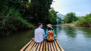 Tayland 'daki Khao Sok Ulusal Parkı' nın sakin sularında süzülen bambu salında iki gezgin dinleniyor. Bereketli yeşilliklerle çevrili doğanın güzelliğinin tadını çıkarıyorlar..