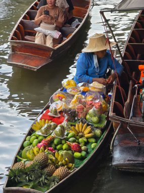 Damnoen Saduak Yüzen Pazarı, Tayland, 5 Aralık 2025. Taze meyve ve sebzelerle dolu renkli tekneler suda süzülüyor. Yerel bir satıcı, tropikal ürünleri ustalıkla sergiliyor.