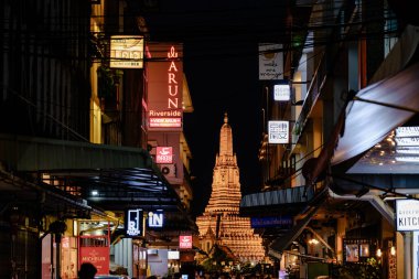 Bangkok, Tayland, 19 Kasım 2025, parıldayan Wat Arun hareketli sokak hayatının ortasında duruyor, gece gökyüzüne karşı aydınlatılmış, şehirde kültür ve modernliğin bir karışımını sergiliyor..