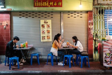 Bangkok, Tayland, 19 Kasım 2025, arkadaşlar Çin Mahallesi 'nde bir sokak kenarı lokantasında toplandılar. Lezzetli yemeklerin ve neon ışıklarının altında taze içkilerin tadını çıkarıyorlar..
