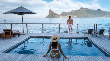 Cape Town, Güney Afrika 'daki en iyi dinlenme yeri. Bir çift, güzel güneşli bir günde, güzel bir masa dağına ve ışıl ışıl okyanusa bakarak, havuz kenarında huzurlu bir günün tadını çıkarıyor..