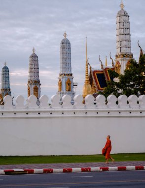 Bangkok, Tayland, 19 Kasım 2025, Wat Phra Kaew yakınlarındaki sakin bir keşiş gün batımında tapınağın karmaşık mimarisi ve altın kuleleriyle çevrili..