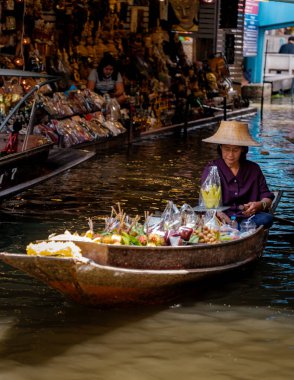 Damnoen Saduak Yüzen Pazarı, Tayland, 5 Aralık 2025. Yerel bir satıcı suda ustalıkla geziniyor, taze meyve ve el yapımı ürünler sunarken, kalabalık piyasa faaliyetleriyle çevrelenmiş durumda..