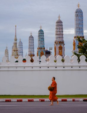 Bangkok, Tayland, 19 Kasım 2025. Huzurlu bir keşiş, bulutlu gökyüzünün altında parlayan büyüleyici tapınak kuleleri ile çevrili, Wat Phra Kaew yakınlarında huzur içinde yürüyor. Tayland 'ın zengin kültürünü somutlaştırıyor..