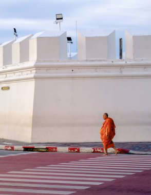 Bangkok, Tayland, 19 Kasım 2025. Canlı turuncu cüppeli yalnız bir keşiş tarihi Wat Phra Kaew yakınlarındaki bir yaya geçidinde yavaşça dolaşarak bölgenin barışçıl atmosferini vurguluyor..