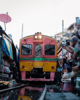 Tayland 'daki Maeklong Demiryolu Pazarı' nın hareketli atmosferini bir trenin kalabalık pazardan geçişini izleyin. Bangkok 'taki demiryolu hattında Taze Pazar, ünlü bir demiryolu pazarı.
