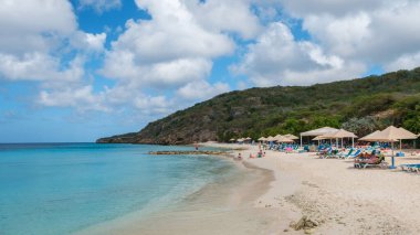 Willemstad, Curacao, 14 Mart 2021. Ziyaretçiler, Curacao 'daki Porto Mari Sahili' nin yumuşak kumlarında güneşleniyorlar. Parlak mavi gökyüzünün altında canlı şemsiyeler var.