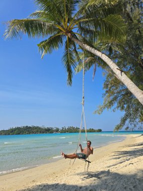 Bir gezgin, Tayland 'ın Koh Kood kentindeki kristal berraklığında sallanan palmiye ağaçlarının altında huzurlu bir anın tadını çıkarır. Bu tropikal sahne cennetin özünü yakalar..