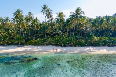 Takhian Sahili 'nin el değmemiş sahillerinde, Koh Kood, Tayland' da, berrak mavi suların gür palmiye ağaçlarıyla buluştuğu yerde rahatlayın. Bir çift adam ve bir kadın gün batımında sahilde, plaj aşıkları