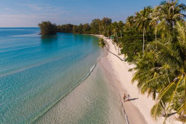 Koh Kood, Tayland 'daki el değmemiş Khlong Hin Sahili' nde güzel bir gün batımının tadını çıkaran bir çift. Sakin turkuaz sular ve sallanan palmiye ağaçları mükemmel bir tatil zemini oluşturur..