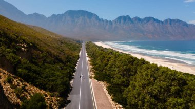 Batı Cape, Güney Afrika 'daki Kogelbay Beach yolu boyunca nefes kesici manzarayı keşfedin. Bereketli yeşillik, açık mavi gökyüzünün altında altın kumlarla buluşur. Gezginleri ve maceraperest arayıcıları davet eder..