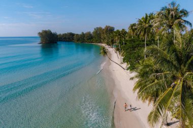 Tayland 'ın Koh Kood kentindeki Khlong Hin Plajı' nda güneşli bir günün tadını çıkarın. Yumuşak kumlar ve canlı palmiye ağaçları bu tropik cennete rahatlama ve macera getiriyor. Kumsalda bir çift yürüyor.