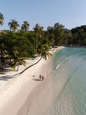Bir çift, Khlong Hin Sahili 'nin sakin kıyı şeridi boyunca el ele yürür. Tayland' da güneşli bir günde yumuşak kum ve hafif dalgaların tadını çıkarırlar..