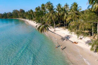 Ziyaretçiler, güneşli bir günde sallanan palmiye ağaçları ve el değmemiş kumlu kıyılarla çevrili Tayland 'ın Koh Kood kentindeki Khlong Hin Sahili' nin sakin sularının tadını çıkarıyorlar..