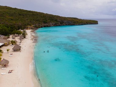 Curacao 'daki Cas Abao Sahili' nde palmiye ağaçları ve canlı turkuaz sularla kaplı yumuşak beyaz kumlar sergileniyor. Ziyaretçiler, parçalı bulutlu bir gökyüzü altında çeşitli aktivitelerden hoşlanırlar. Tropik bir kaçış için mükemmel bir yer..