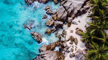 El değmemiş turkuaz sular Anse Patates 'in kumlu kıyılarını kucaklayarak pürüzsüz kayaları ve gür palmiye ağaçlarını ortaya çıkarıyor. Kumsaldaki bir çiftin İHA üst görüntüsü, La Digue, Seyşeller.