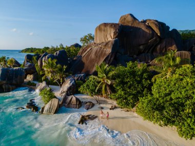 Anse Source d 'Argent' ın el değmemiş kıyılarında gezinen bir çift, iki gezgin, La Digue, Seyşeller 'deki dev granit kayalar ve turkuaz sularıyla çarpıcı manzaranın tadını çıkarıyorlar.