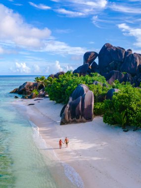 Çift, Anse Source d 'Argent sahilinin el değmemiş kumlarında romantik bir yürüyüş yapıyor. Güzel bir günbatımında, La Digue, Seyşeller' deki büyüleyici granit kayalar ve yemyeşil alanlarla çevrili..
