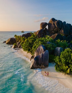 Güneş Seyşeller 'in sakin sularında batarken görkemli granit kayalar ve yemyeşil yeşilliklerle çevrili el değmemiş Anse Kaynak d' Argent plajı boyunca romantik bir gezinti yapıyorlar..