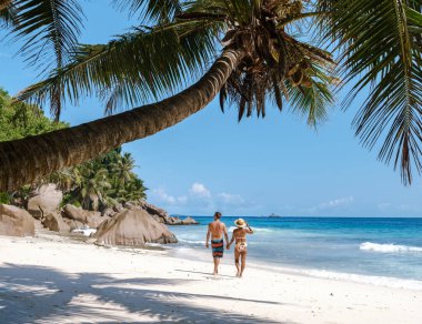 Çift el ele yürür Anse Patates 'in el değmemiş beyaz kumları boyunca, sıcak güneşin ve turkuaz denizin yumuşak dalgalarının tadını çıkarırlar. La Digue, Seyşeller