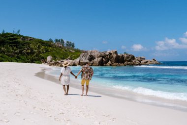 İki kişi el ele yürür Anse Cocos sahilinin el değmemiş beyaz kumlarında, güneşin altında ve turkuaz dalgalarda. La Digue, Seyşeller 'deki bu güzel yer romantik bir kaçamak için mükemmel..
