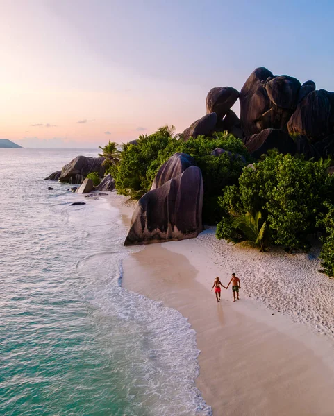Çift, Seyşeller 'in La Digue kentindeki Anse Source d' Argent plajında romantik bir akşam gezintisi yapıyor. Güneş muhteşem granit kayaların arkasında batar ve büyülü bir atmosfer yaratır..