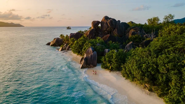 La Digue 'deki Anse Source d' Argent plajında yumuşak dalgalar çakışıyor. Yükselen granit kayalar canlı bir günbatımının arka planında duruyor, La Digue, Seyşeller