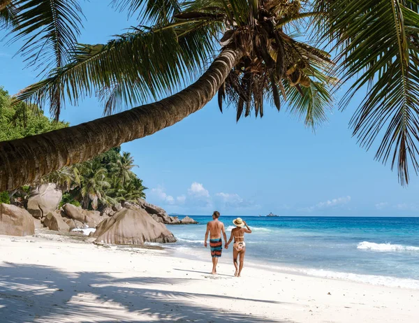 Çift el ele yürür Anse Patates 'in el değmemiş beyaz kumları boyunca, sıcak güneşin ve turkuaz denizin yumuşak dalgalarının tadını çıkarırlar. La Digue, Seyşeller